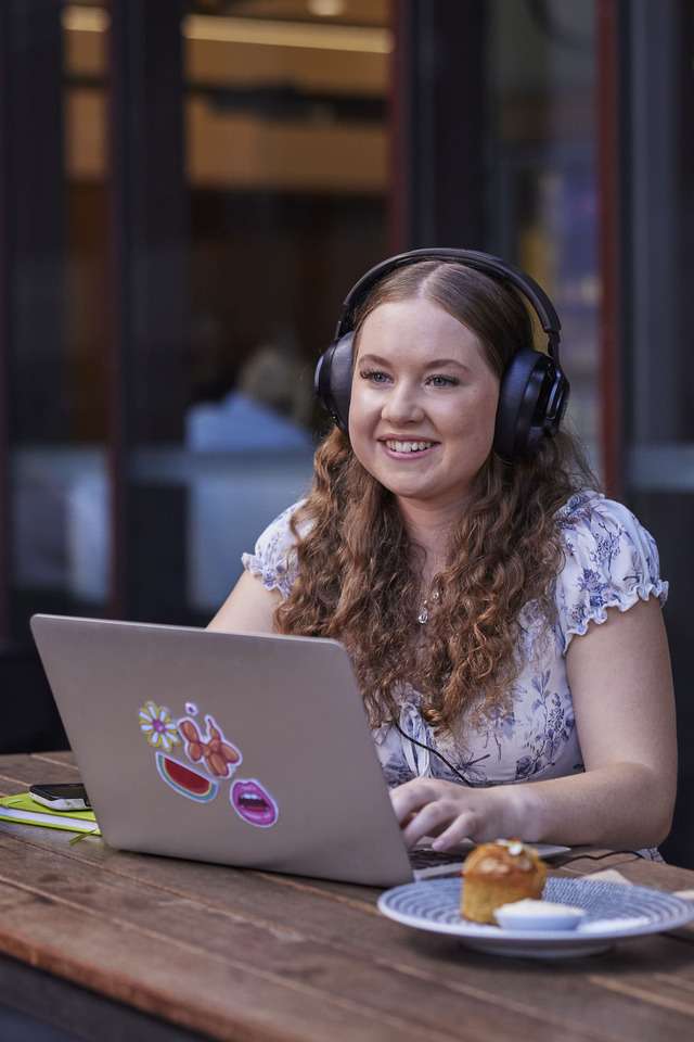 High School student sitting outside a cafe with a laptop and headphones studying
