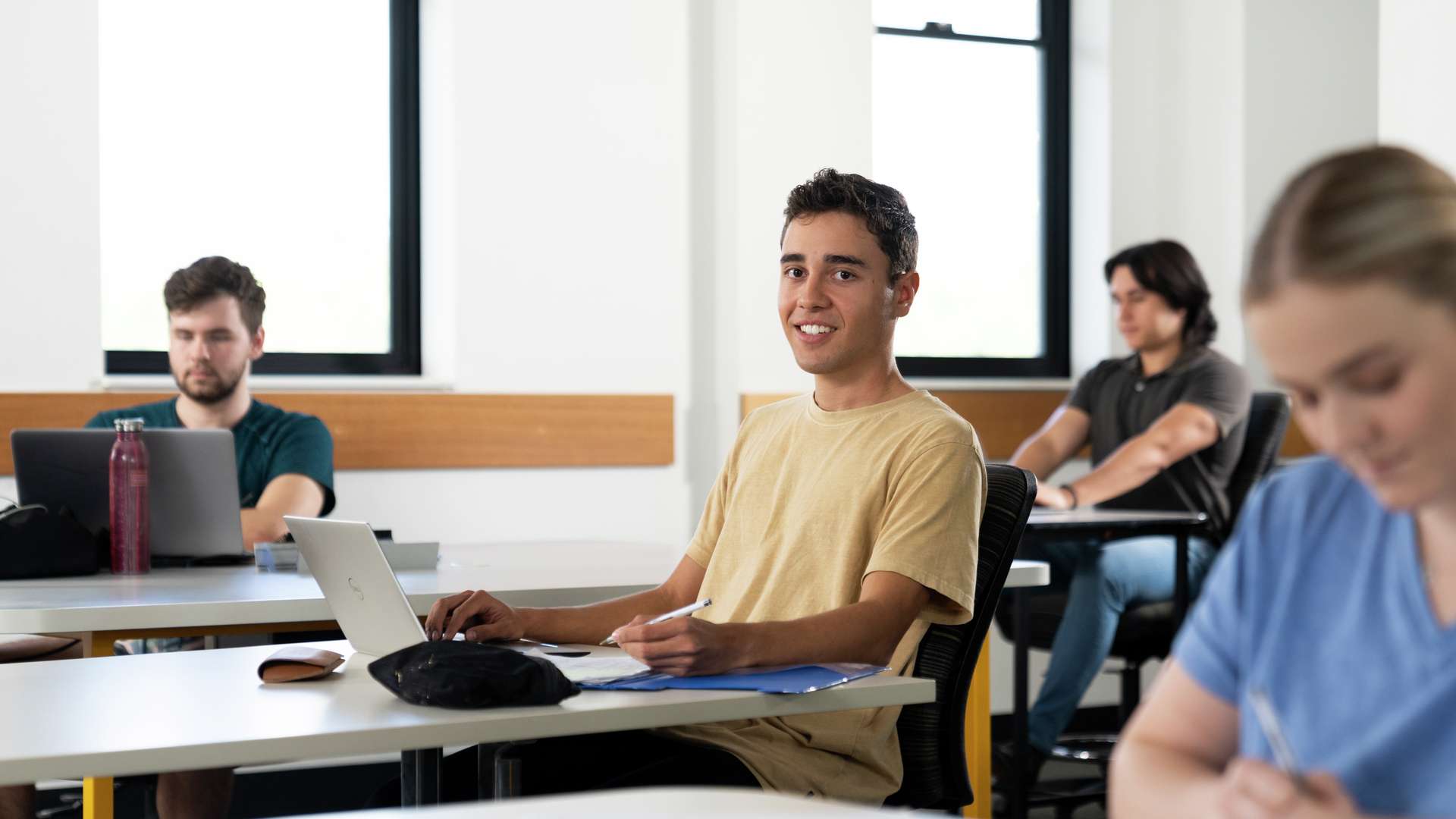 Student in classroom with other students smiling at the camera.