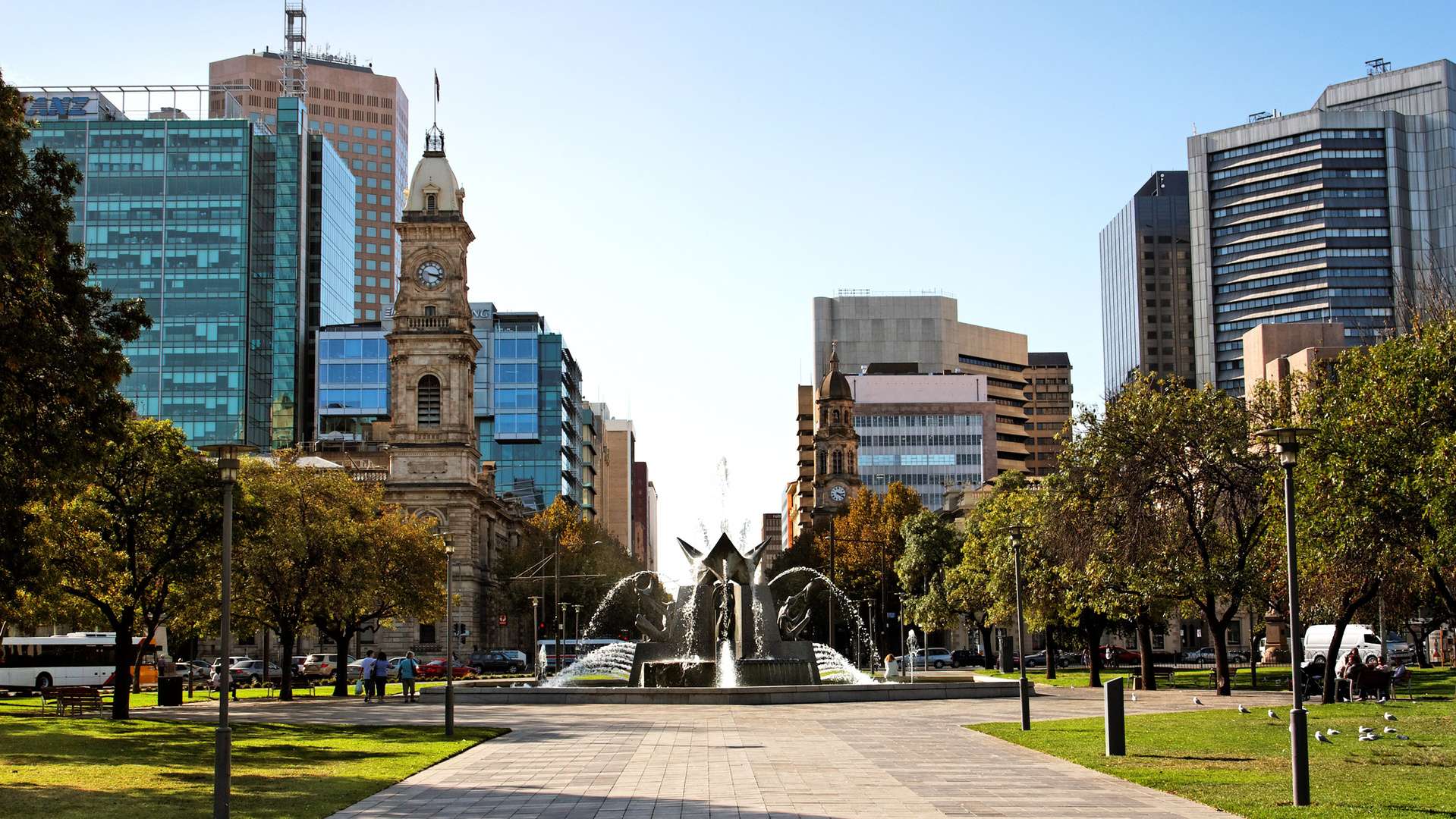 Victoria Square in Adelaide, a fountain can be seen with parkland to either side, and buildings in the background.