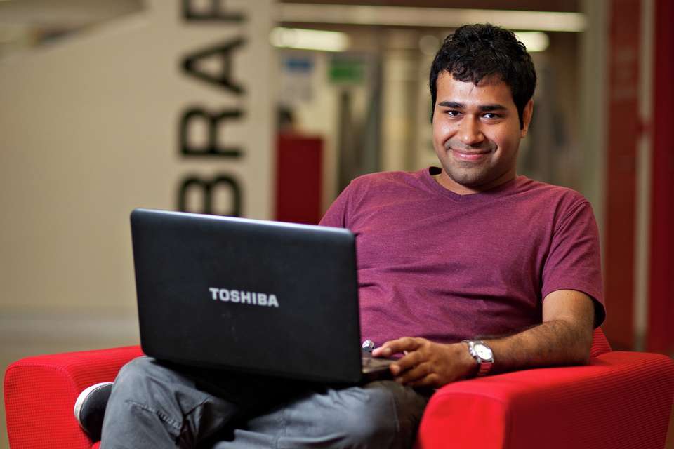 Student sits in a chair on campus while working on a laptop.