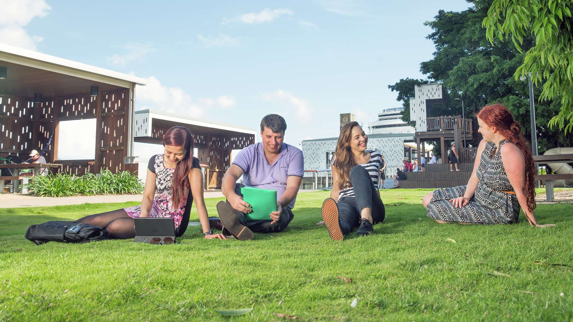 CQU students sitting, chatting and studying on the grass under a blue sky on campus