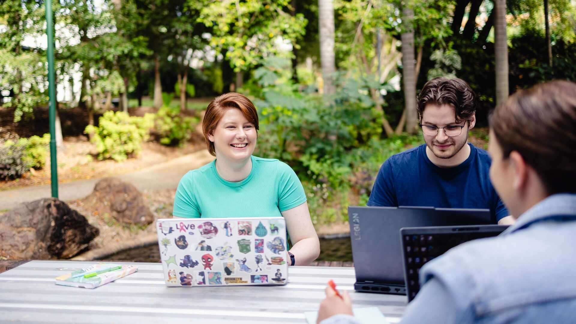 Two CQU TAFE students sit at a table facing the camera while working on their computers, a third student has their back to the camera.