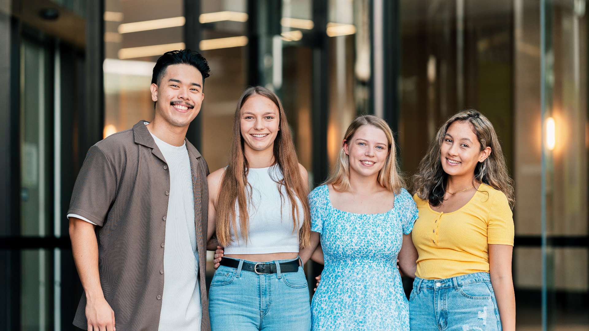 Four high school students standing together infront of a glass building smiling