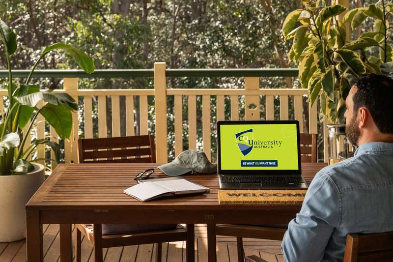 Student sitting on veranda studying online with a laptop showing CQUniversity logo