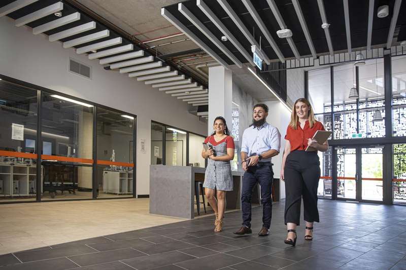 Three students walking through modern building with notepads