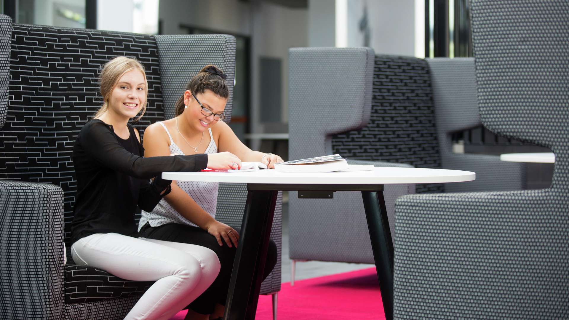 Two students sitting on a bench seat at a table studying together.