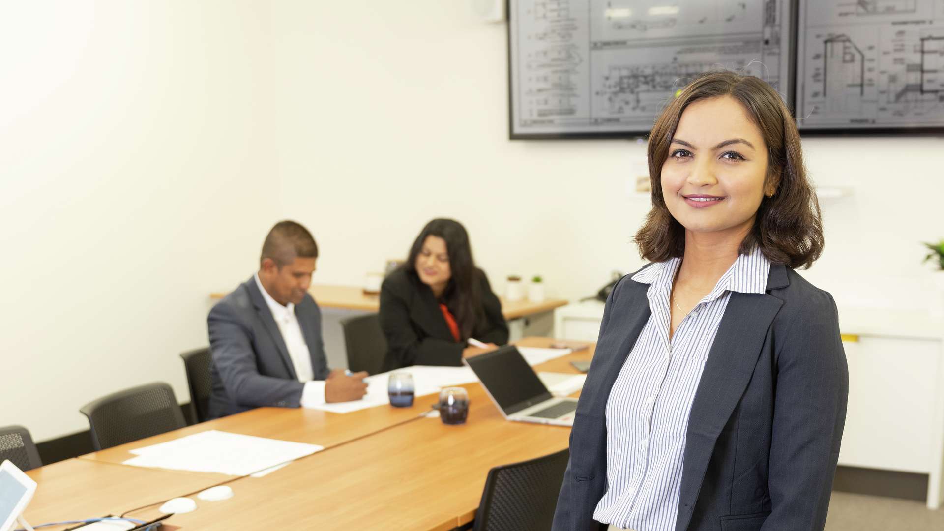 Construction management student holding paperwork with two colleagues sitting at board table in background.
