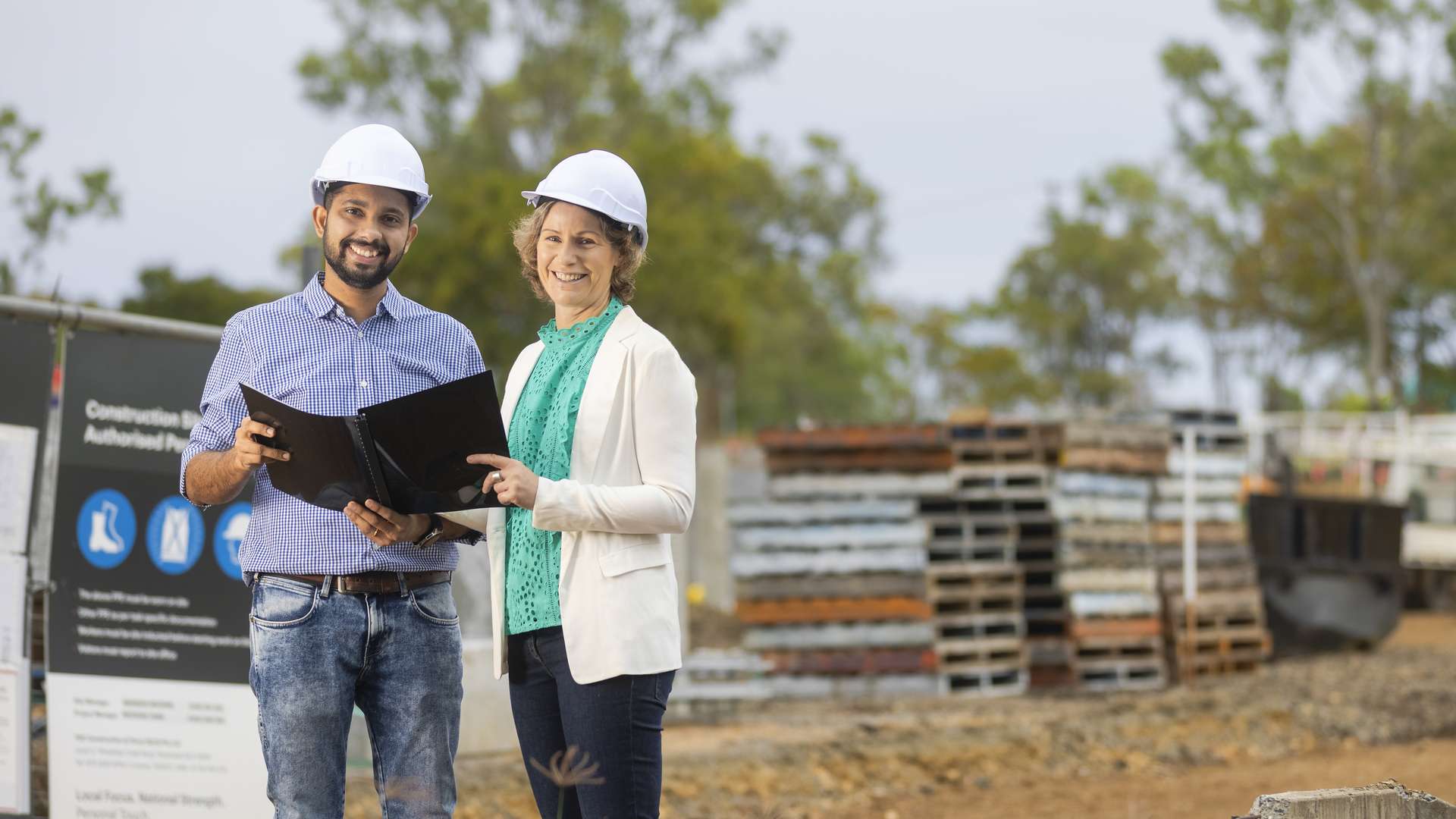 An international student and their trainer standing on a construction site holding plans
