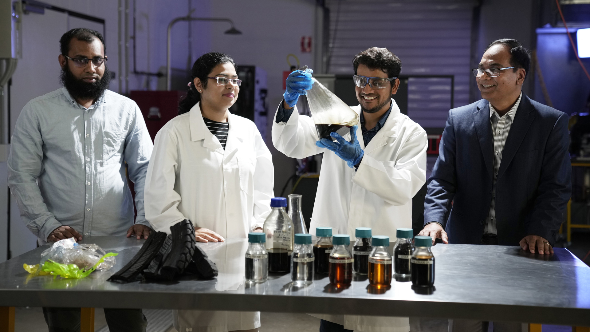 Three engineering students looking at chemicals in a lab with teacher.