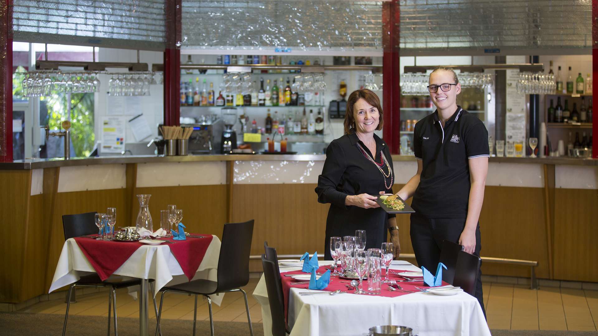 A hospitality teacher holding a plate of food with a student in a restaurant