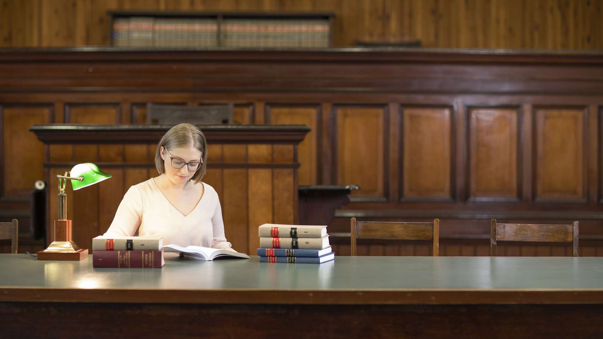 A student sits at a large table surrounded by stacks of Law books. The student has a book open and is reading it.