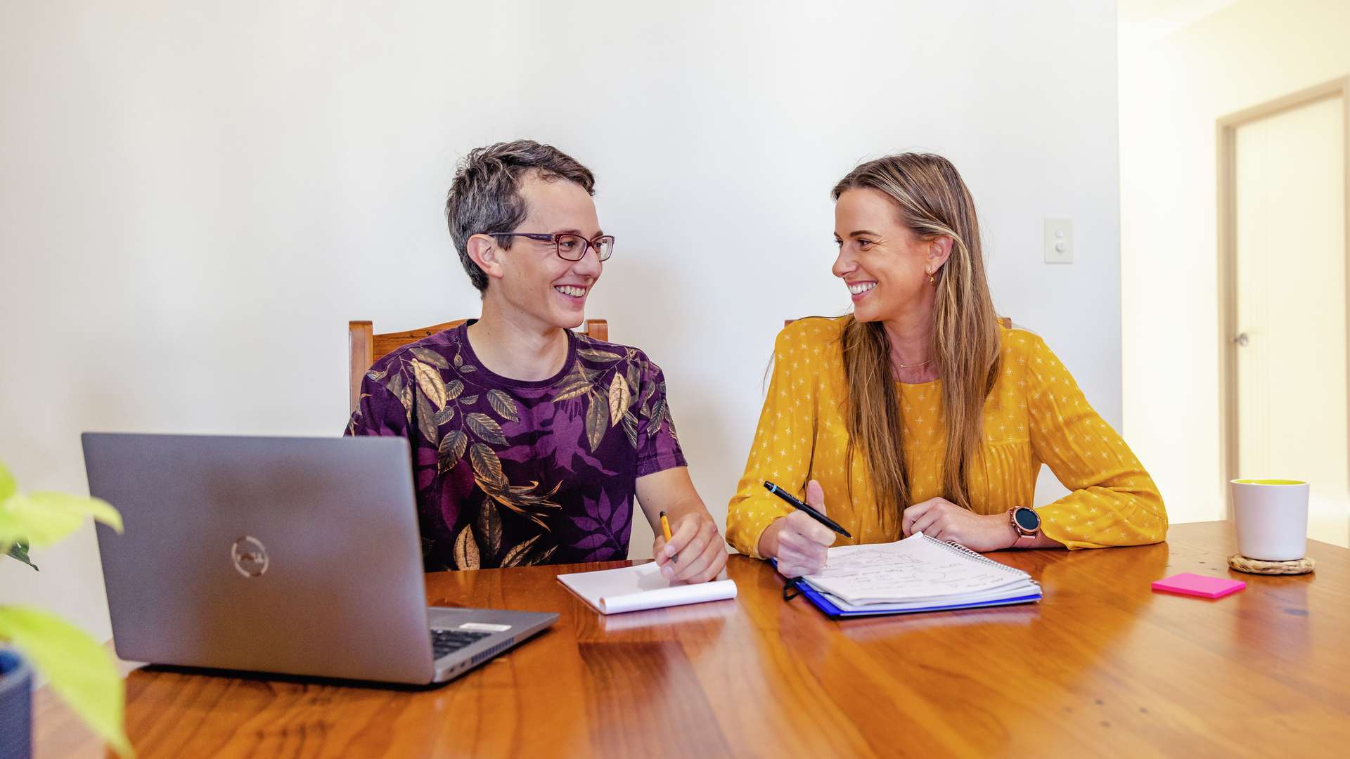 Two happy students taking notes while studying online from home with a laptop