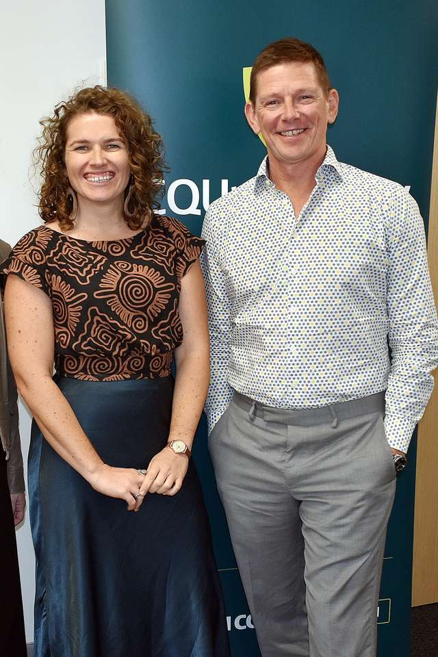 Three people standing together smiling in front of CQU sign.